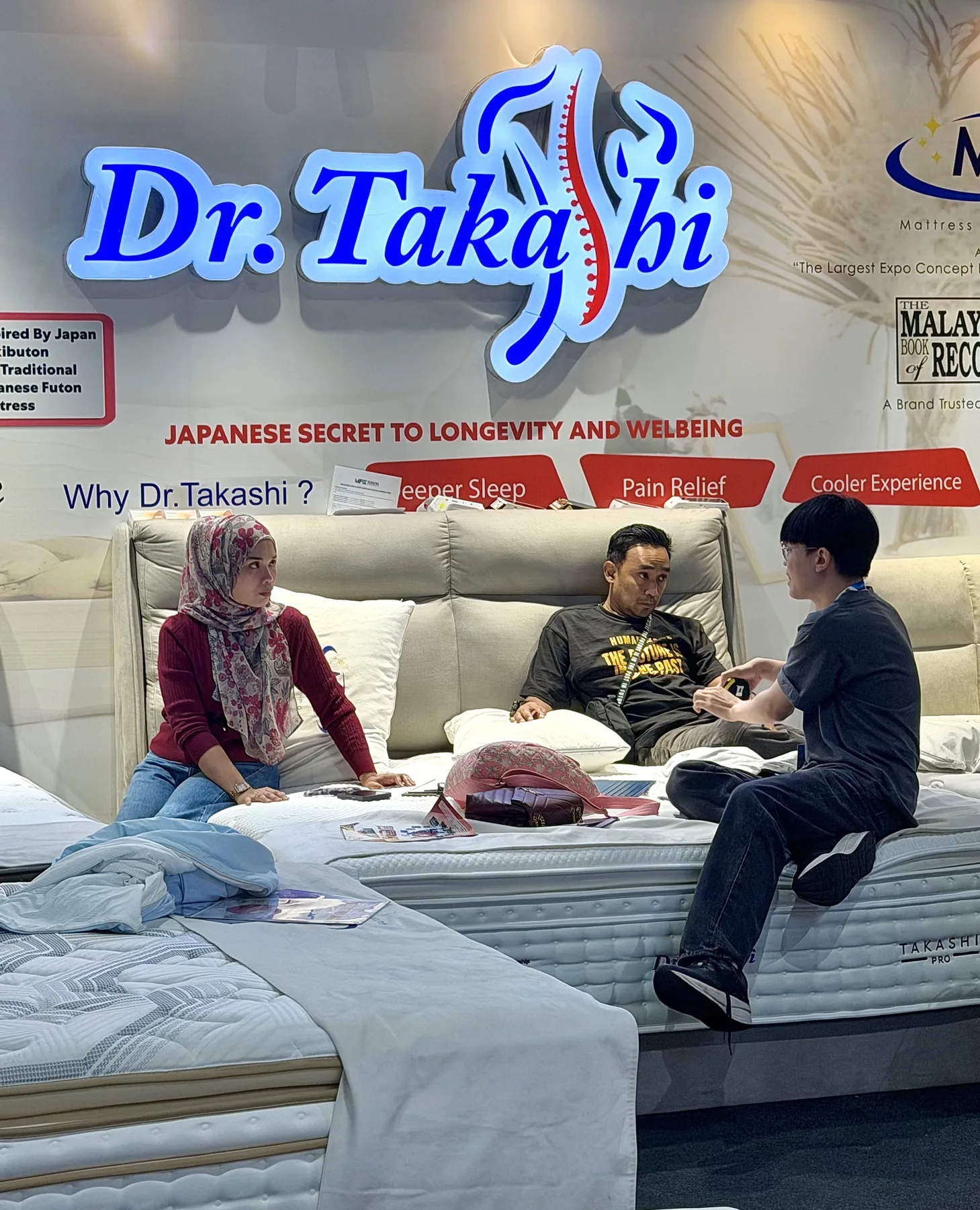 Visitors experiencing the comfort of Dr. Takashi mattresses at an exhibition booth.